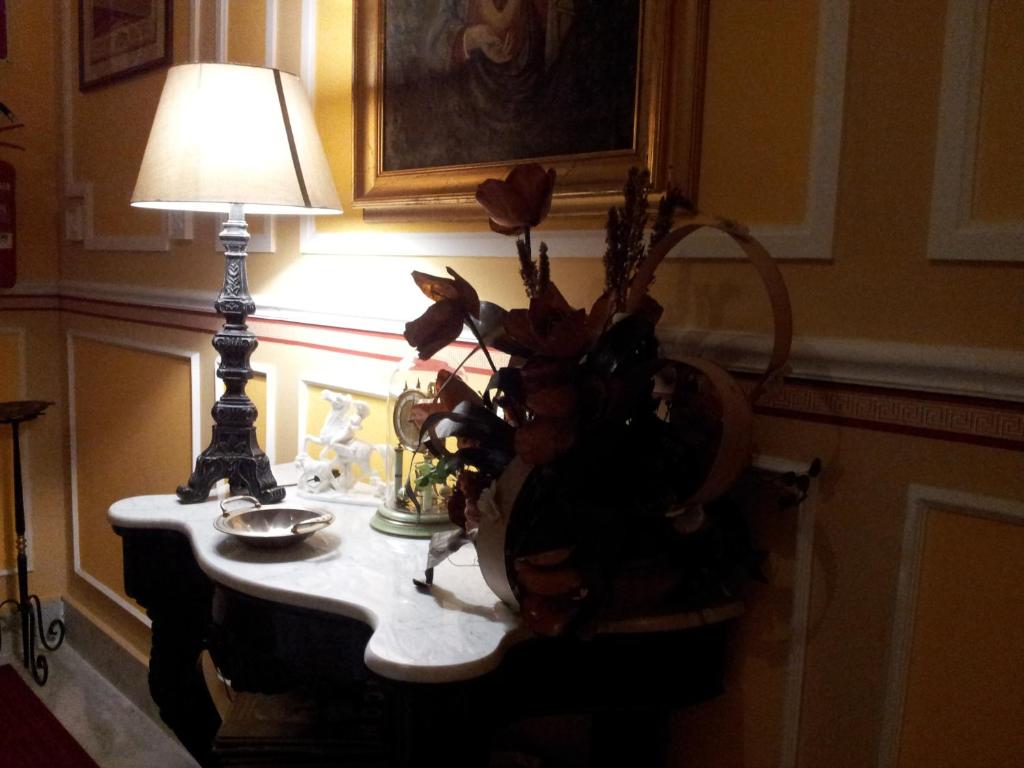 un tavolo con una lampada e un vaso di fiori sopra di Hotel Amadeus a Caserta