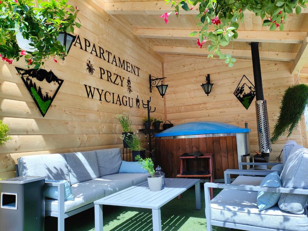 a patio with a couch and tables and a wooden wall at Apartament przy Wyciągu z jacuzzi in Bukowina Tatrzańska
