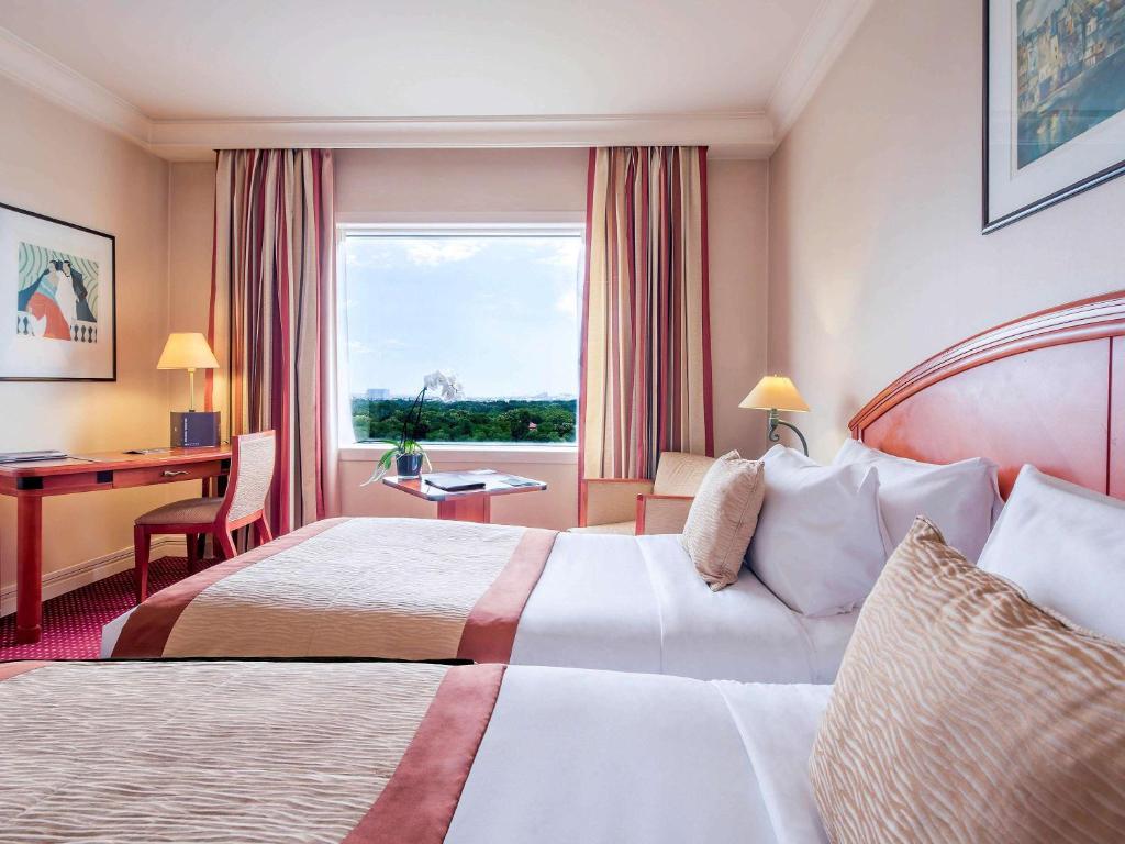 a hotel room with two beds and a desk and a window at Pullman Bucharest World Trade Center in Bucharest
