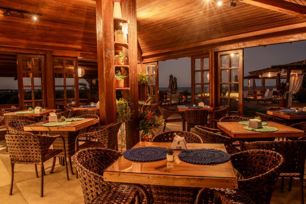 a restaurant with wooden tables and chairs and windows at Manacá Pousada Parque in Arraial d'Ajuda