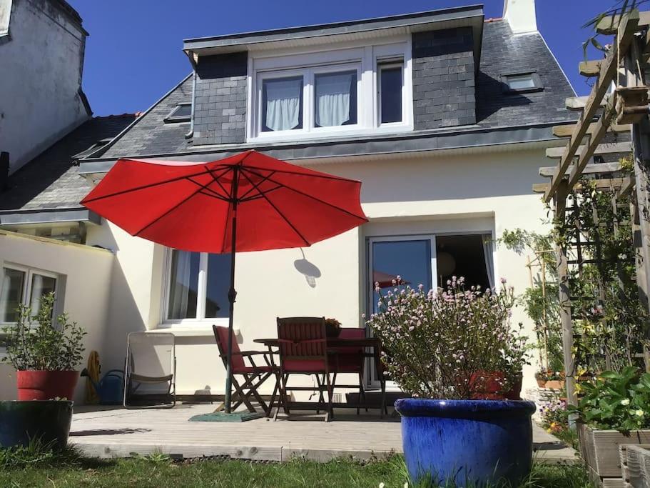 un parasol rouge, une table et des chaises devant une maison dans l'établissement Jolie Maison proche plage Sables Blancs, à Concarneau