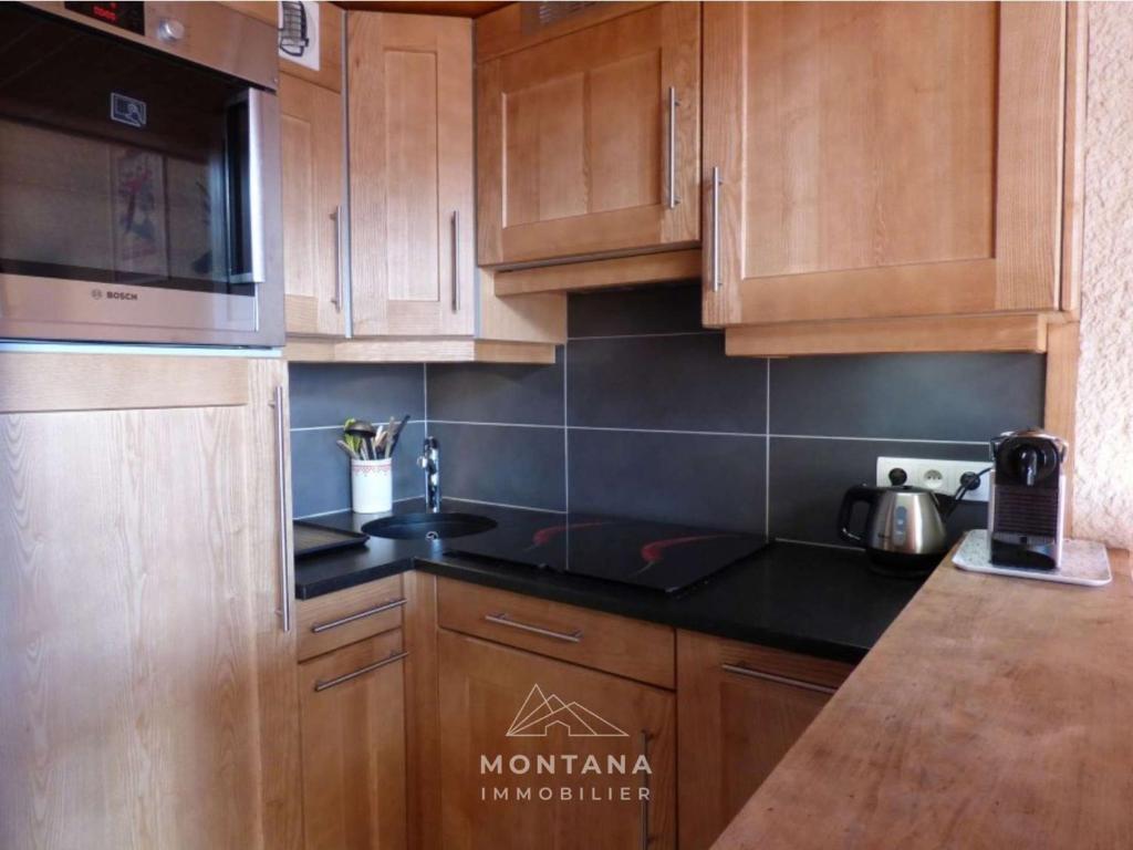 une cuisine avec des placards en bois et des comptoirs noirs dans l'établissement Agréable appartement montagnard pour 6 pers. proche commerces et télécabines - FR-1-458-149, au Grand-Bornand