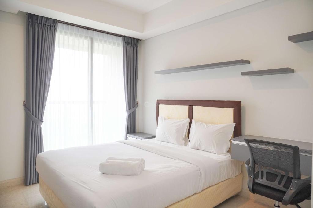 a bedroom with a white bed with a desk and a chair at Minimalist and Nice Studio at Gold Coast Apartment By Travelio in Jakarta