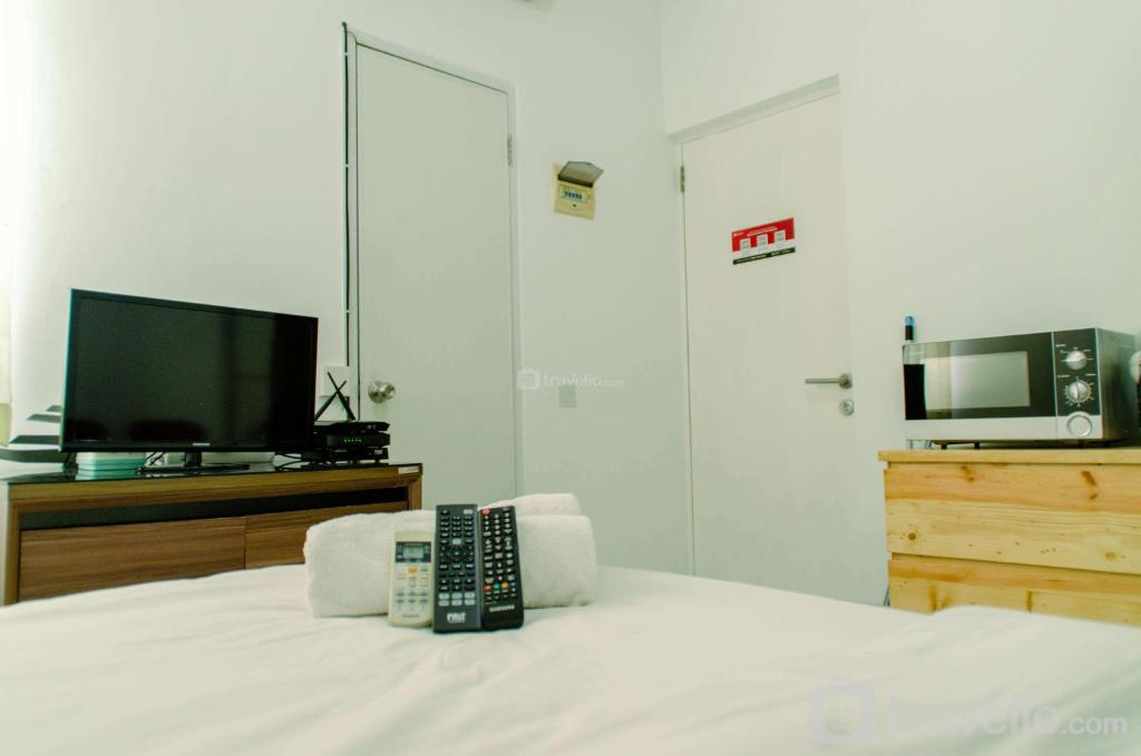 a bedroom with a television and a remote control on a bed at Comfort Studio Apartment Aeropolis Residence By Travelio in Tangerang
