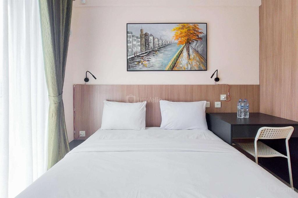 a bedroom with a bed and a desk and a painting at Comfy and Best Choice Studio at Sky House BSD Apartment By Travelio in Tangerang