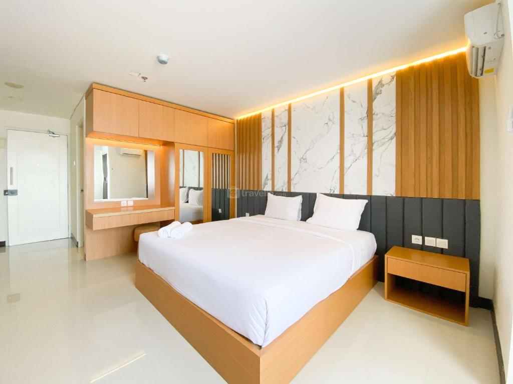 a bedroom with a large white bed and a mirror at Homey and Strategic Studio (No Kitchen) at Sentraland Semarang Apartment By Travelio in Semarang