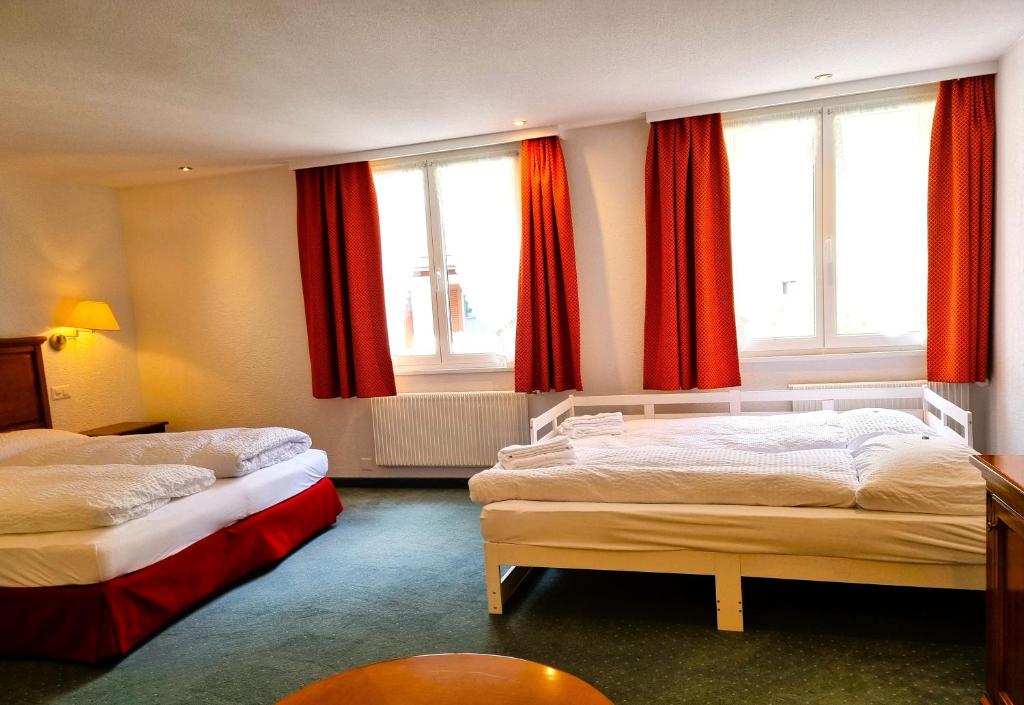a hotel room with two beds and red curtains at Self-Service Guesthouse Berggeist in Saas-Fee