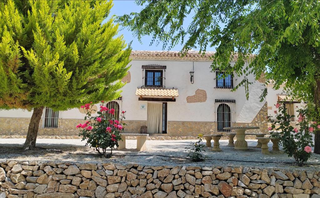 a house with a stone wall and trees in front of it at La Noguera Casa Rural in Huéscar