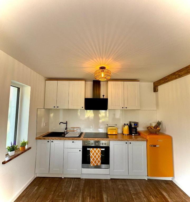 a kitchen with white cabinets and an orange stove at Ganzes Tiny House "Thüringer Ruhe" mit großem Garten nahe Rennsteig in Laucha