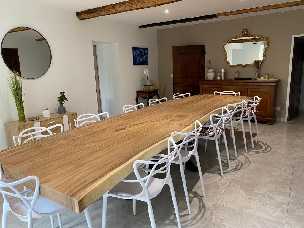 une grande table en bois avec des chaises blanches dans une pièce dans l'établissement Maison de la tuilière hautes alpes piscine et boulodrome 12 personnes, à Saléon