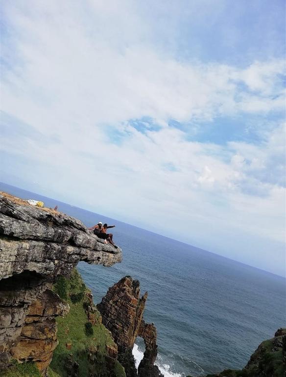 un gruppo di persone sedute su una scogliera che domina l'oceano di Mbotyi Mnceba cottage a Lusikisiki