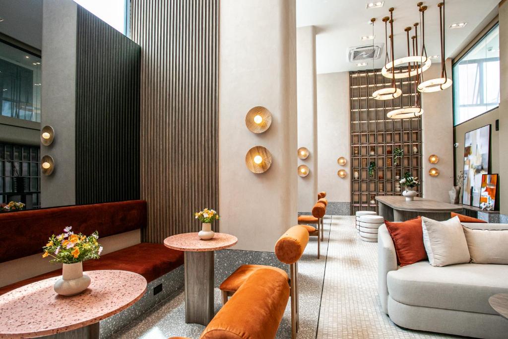 A bright hotel lobby lounge with velvet seating, round tables and sculptural pendant lights.