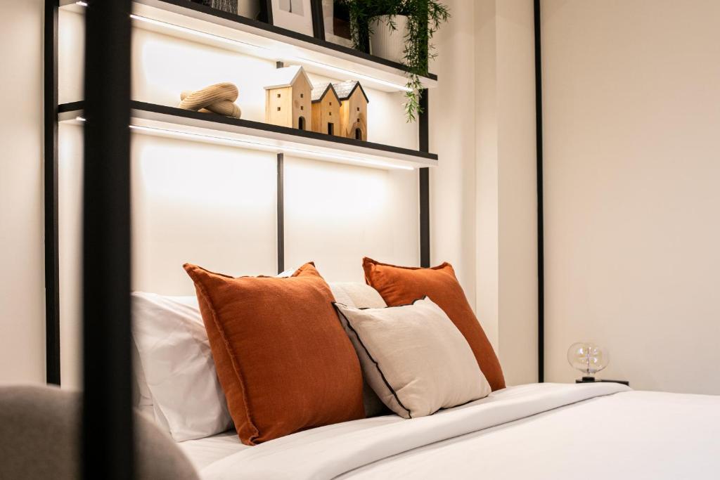 A styled bed with orange and white cushions beneath illuminated display shelves.