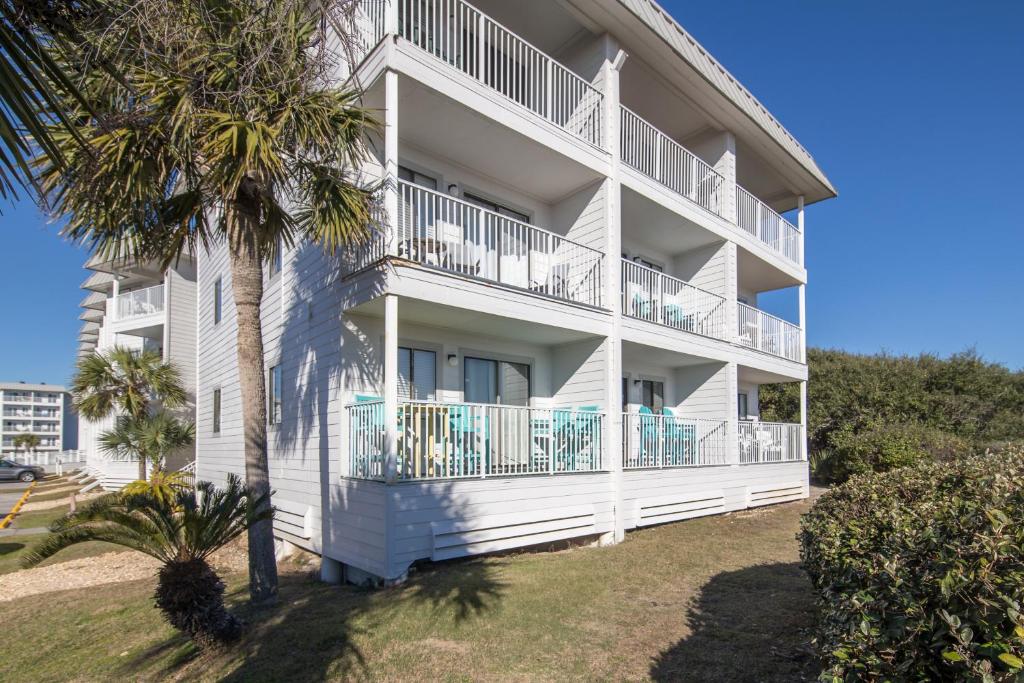 a white building with balconies and a palm tree at Plantation Condos in Gulf Shores