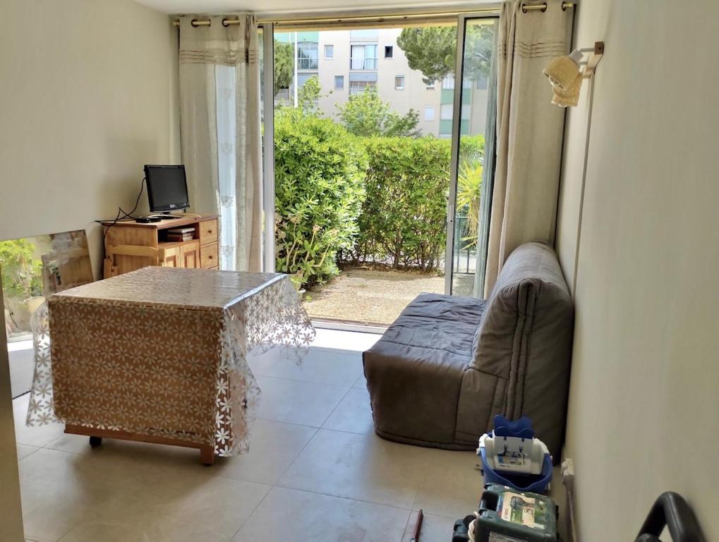 Una sala de estar con un sofá y una mesa y una ventana. en Le Regina Studio 5p mer parking, en Le Grau-du-Roi