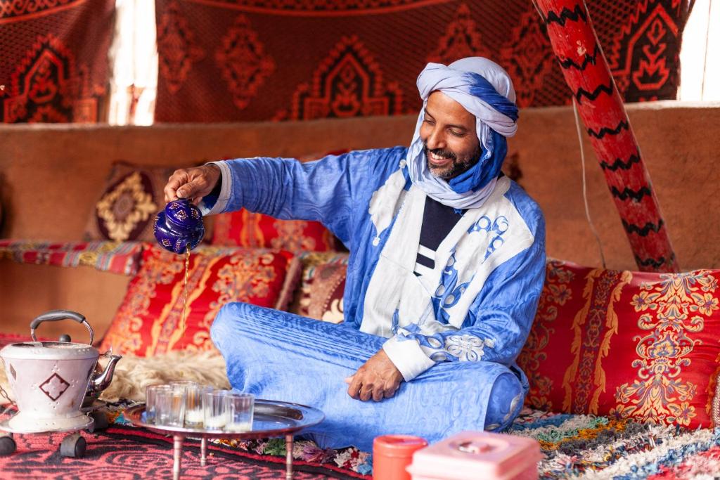 a man sitting on a bed holding a bottle at La Maison de l'Homme Bleu in Tighmert