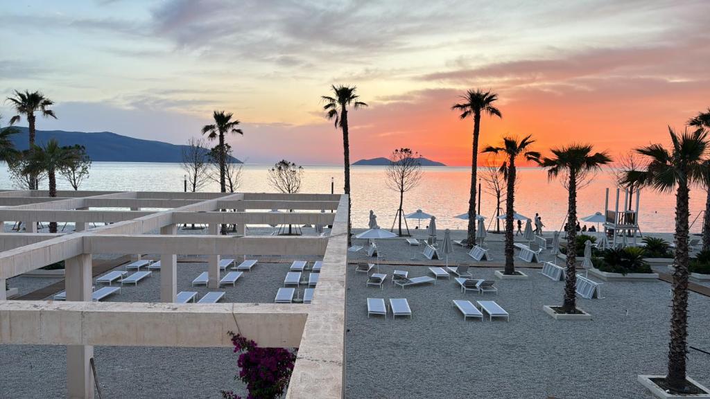 a beach with chairs and palm trees at sunset at SoleMar Suites in Vlorë