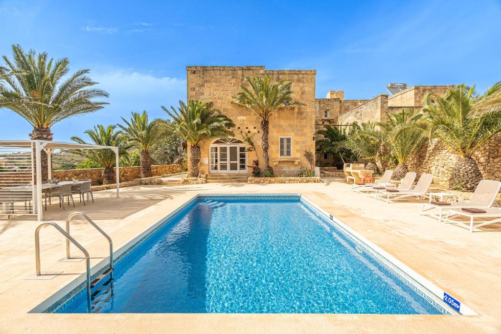 a pool in front of a house with palm trees at Sinjura Holiday Home in Xagħra
