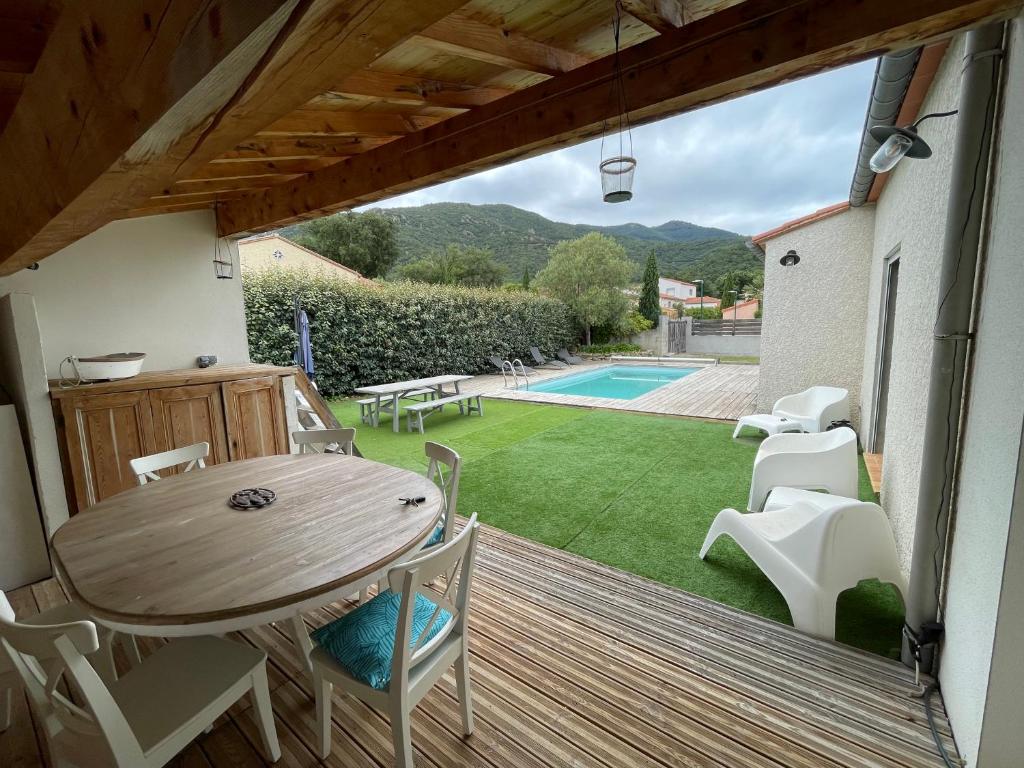 une terrasse en bois avec une table et des chaises ainsi qu'une piscine dans l'établissement Maison avec piscine entre plage et montagne, à Laroque-des-Albères