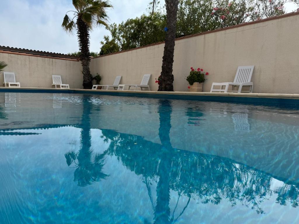 une piscine d'eau avec des chaises et des palmiers dans l'établissement Résidence la piscine, au Barcarès