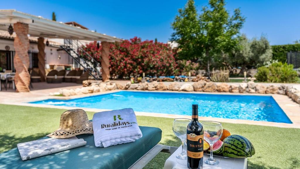 a table with wine bottles and glasses next to a swimming pool at Capricho de Luna Atarfe by Ruralidays in Atarfe