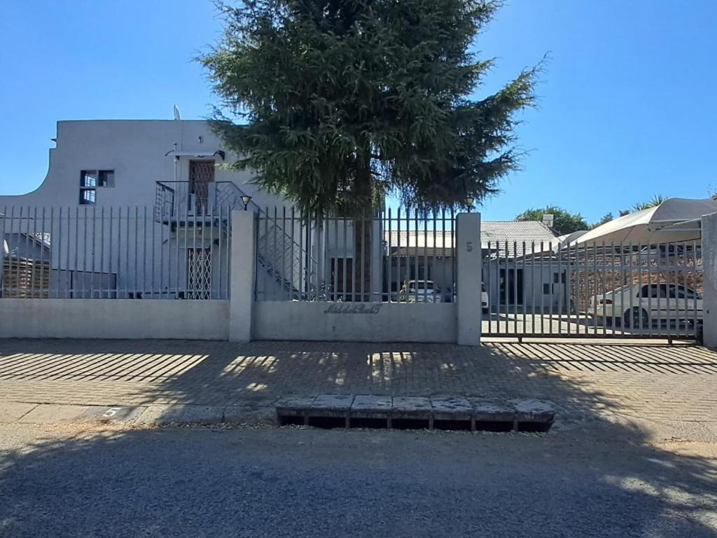 a white fence with a tree in front of a building at Middelbult Guesthouse by Heybert in Secunda