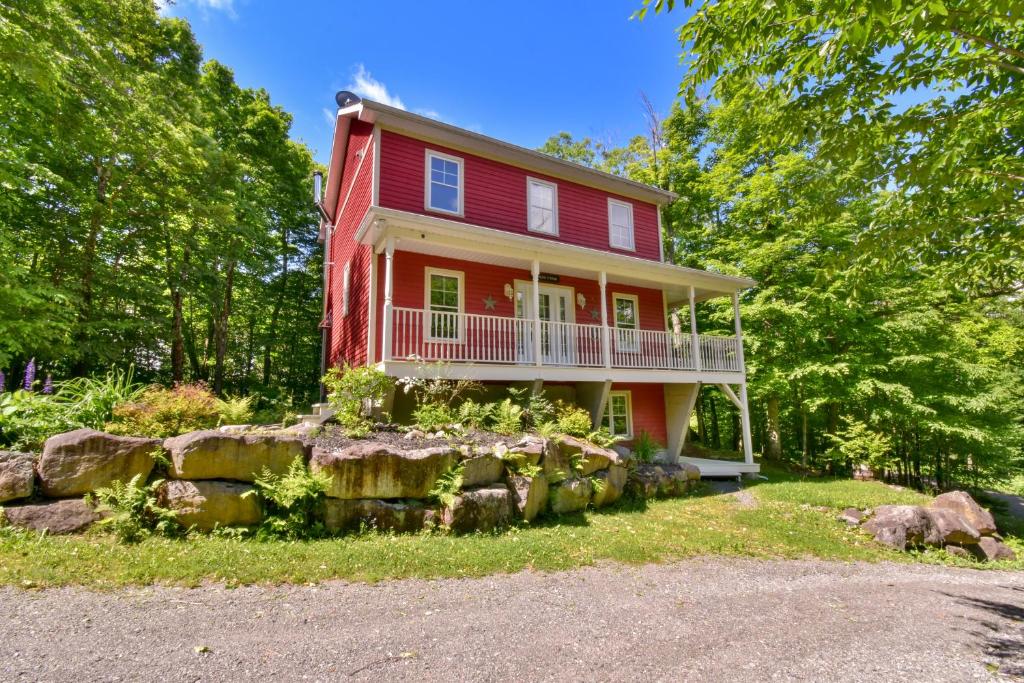 a red house with a balcony and a yard at Nature retreat with HOT TUB and lake access & watercraft in Saint Adolphe D'Howard