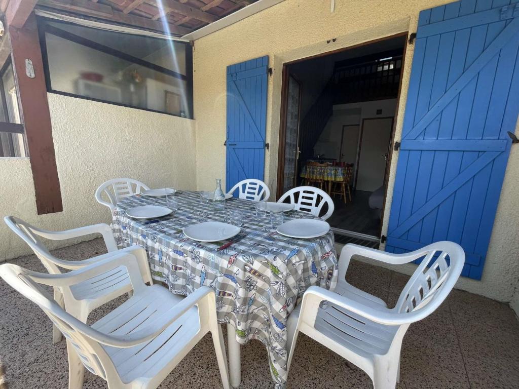une table avec des chaises blanches et une porte bleue dans l'établissement Villa T2 Mezzanine, Parking, Proche Plage, 6 Pers – Terrasse Lumineuse et Équipements Complets - FR-1-795-31, à Fleury