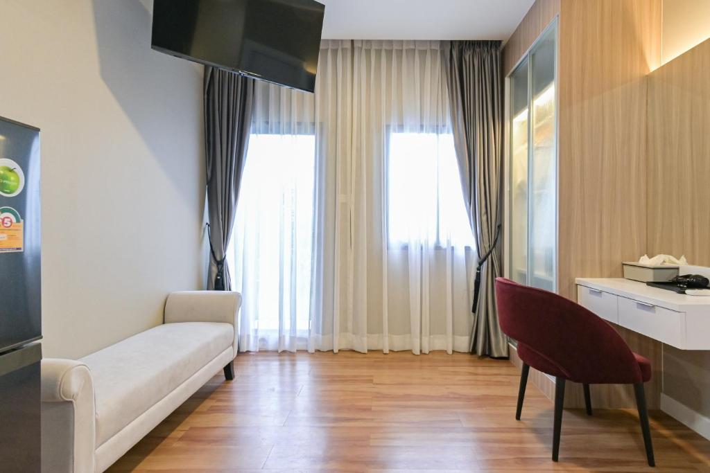 A living area with a white sofa, desk, chair, television and tall curtained windows.