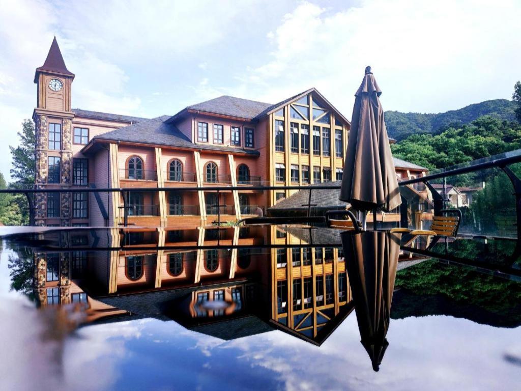 Un edificio con una torre de reloj y una sombrilla en el agua. en Beijng Chestnut Valley Hotel, en Sanduhe