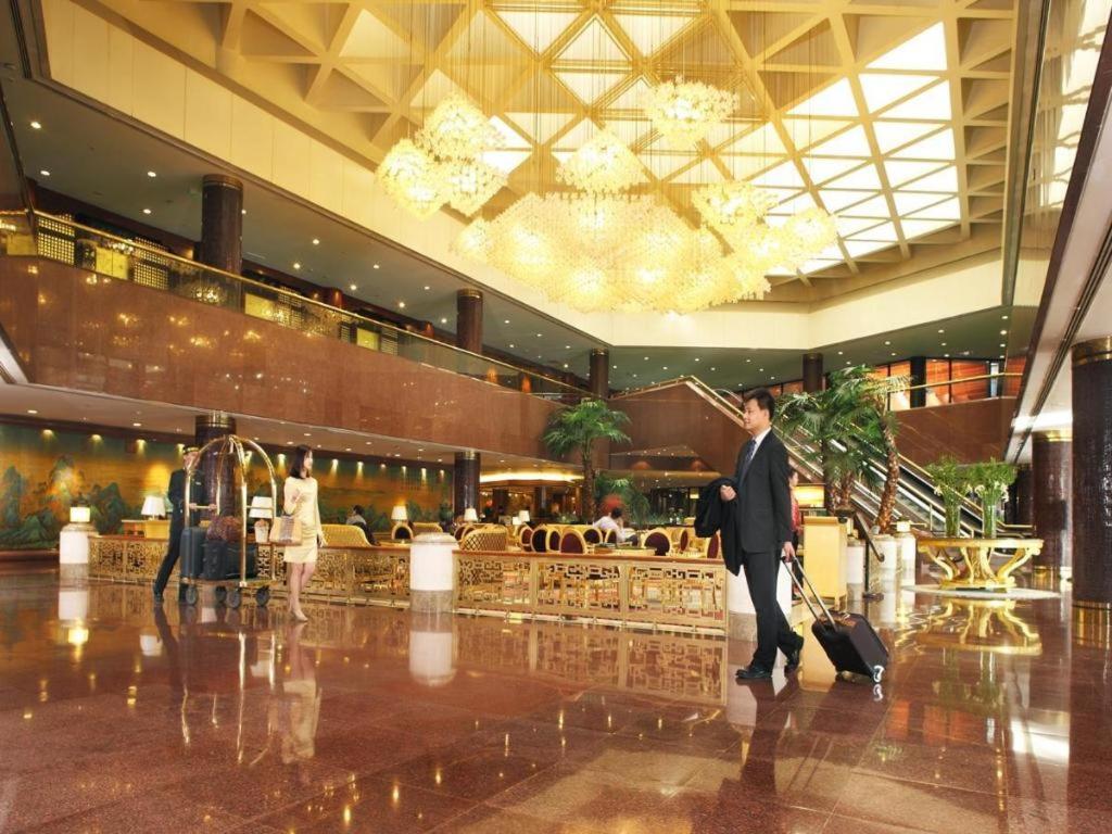 un uomo che cammina nella hall di un hotel con i bagagli di Capital Hotel a Pechino