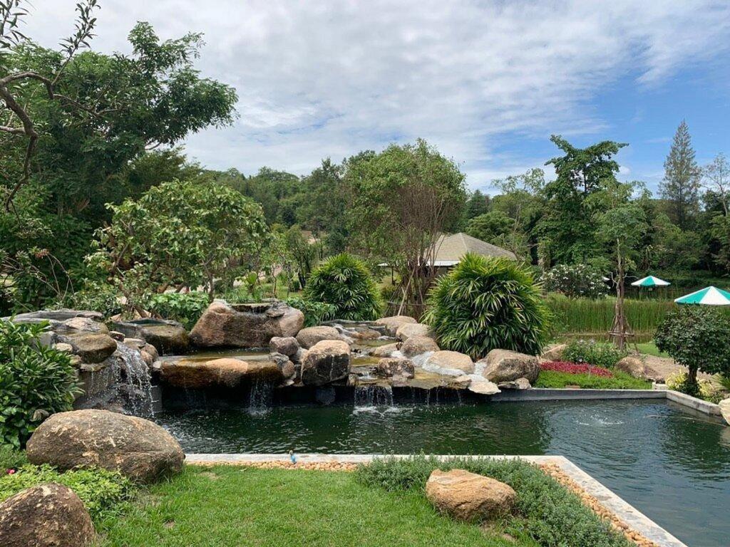 a pond with a waterfall in a garden with rocks at Greenfield Valley Fishing Resort in Hua Hin