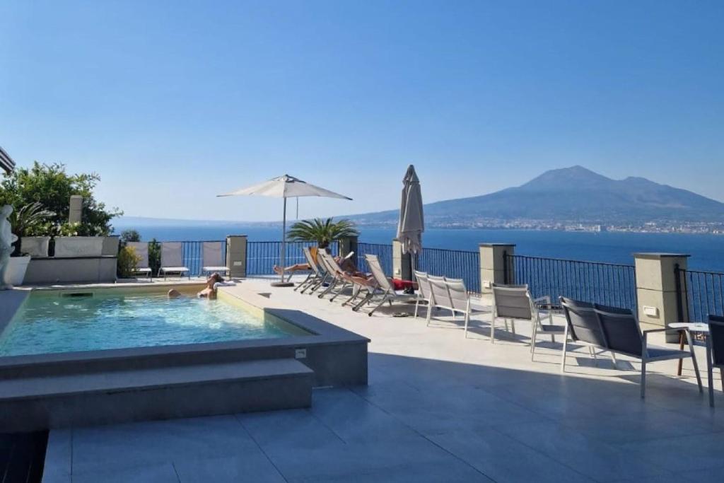 a swimming pool with chairs and umbrellas and the ocean at La Panoramica Hotel in Castellammare di Stabia