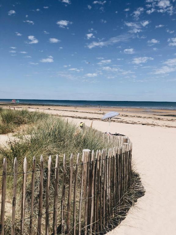 une clôture en bois sur une plage avec un parasol dans l'établissement Maison proche mer, à Courseulles-sur-Mer