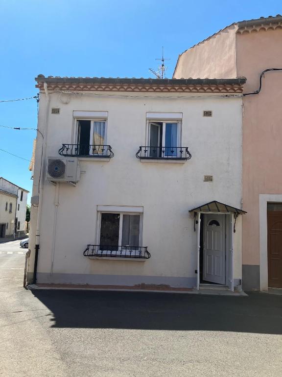 - un bâtiment blanc avec trois fenêtres et une porte dans l'établissement Coquette maison de ville au centre du village - V0787, à Vias