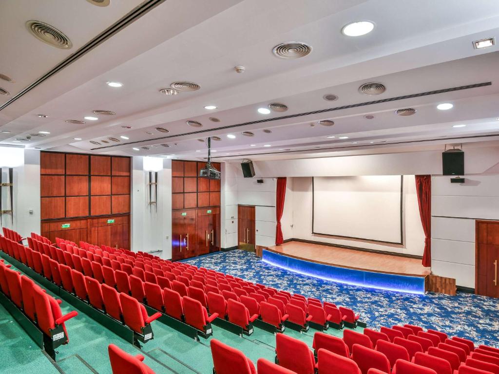 a lecture hall with red chairs and a screen at Pullman Bucharest World Trade Center in Bucharest