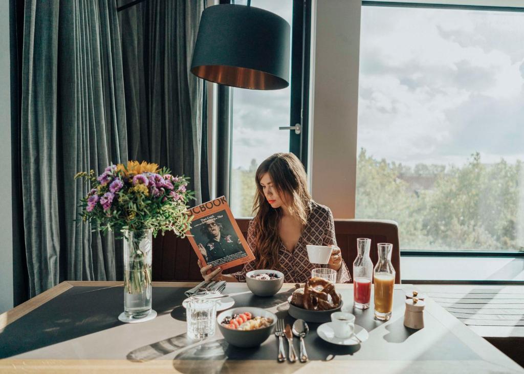Eine Frau, die an einem Tisch sitzt und ein Buch liest. in der Unterkunft Andaz Munich Schwabinger Tor, By Hyatt in München