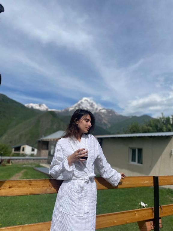 Una mujer parada junto a una valla sosteniendo una copa de vino. en Guest House Elguja Qushashvili, en Kazbegi