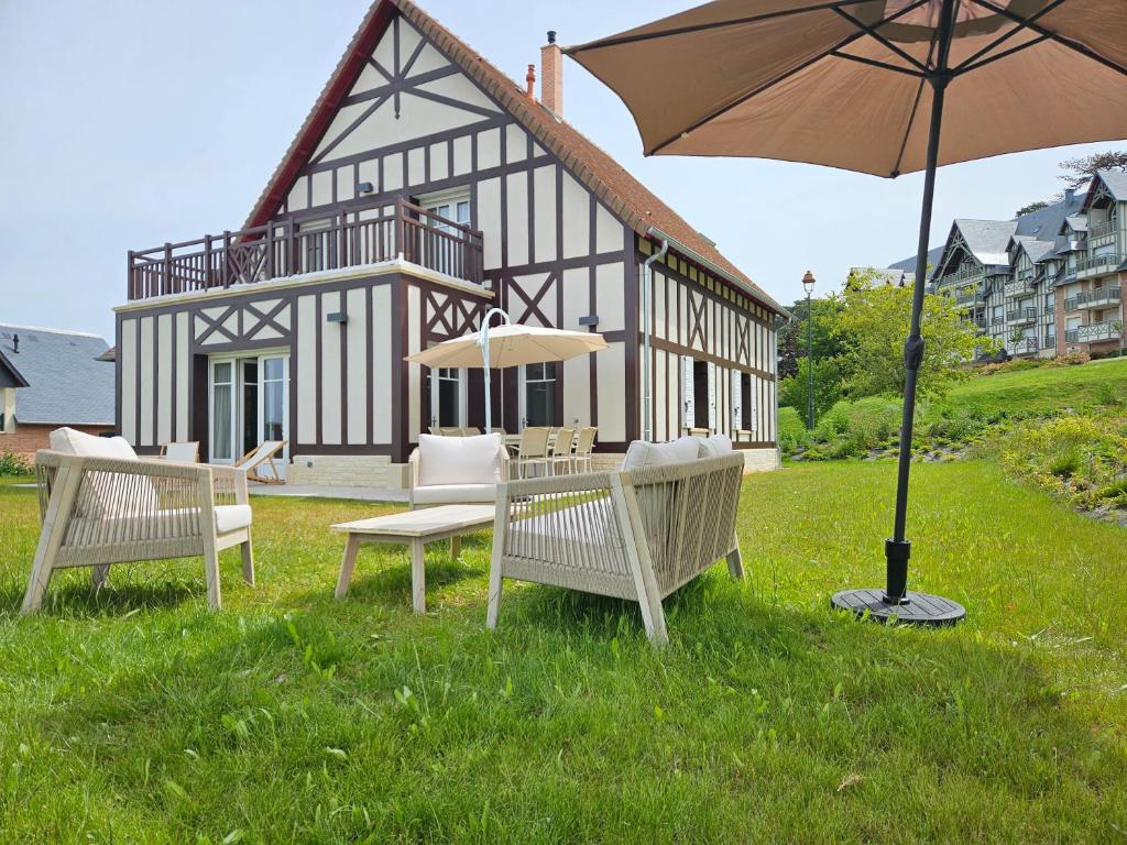 une maison avec des bancs et un parasol dans l'herbe dans l'établissement Superbe villa familiale, 8 couchages, à Deauville
