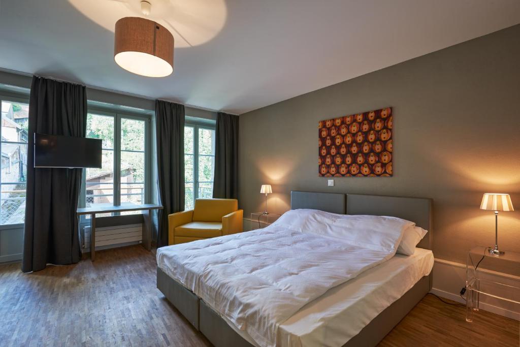 a bedroom with a bed and a chair and windows at Hotel Hine Adon Fribourg in Fribourg