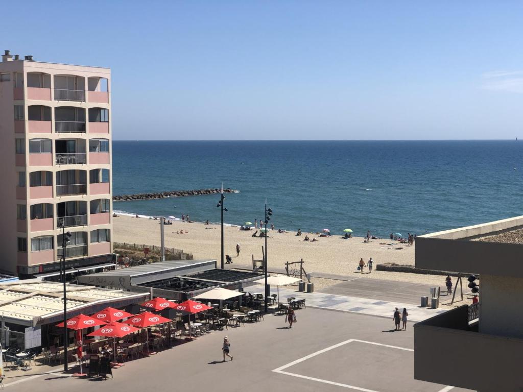 - une plage avec des parasols, un bâtiment et l'océan dans l'établissement Studio Cabine Climat. 4P, Proche Plage, Animaux OK - FR-1-793-23, à Saint-Cyprien