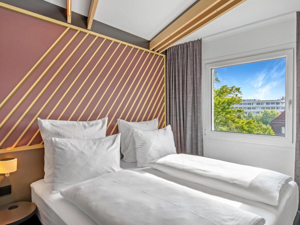 two beds in a hotel room with a window at B&B Hotel Hamburg-Airport in Hamburg
