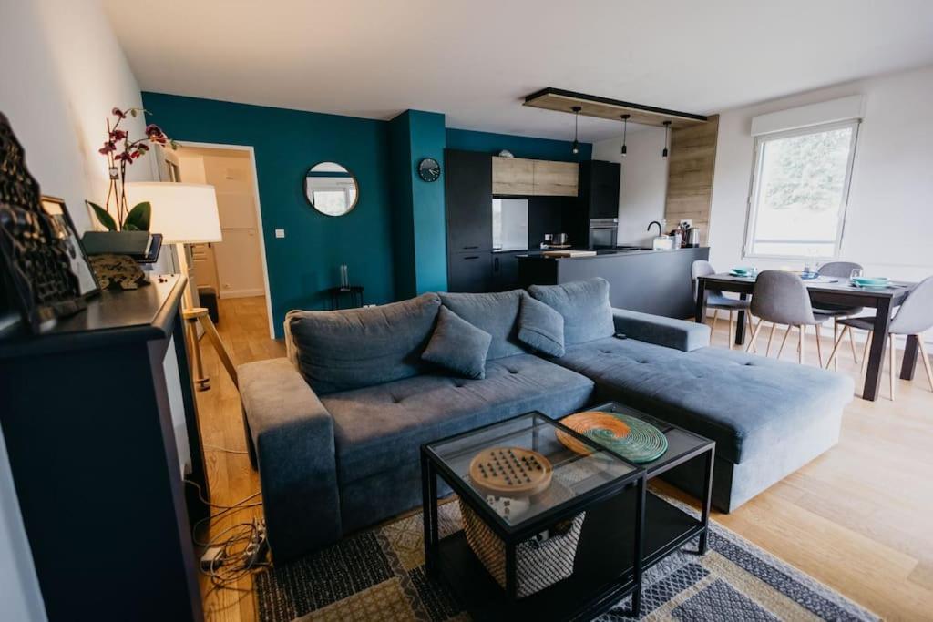 un salon avec un canapé bleu et une cuisine dans l'établissement Appartement cosy avec wifi à 15 min de Rennes, à Crévin