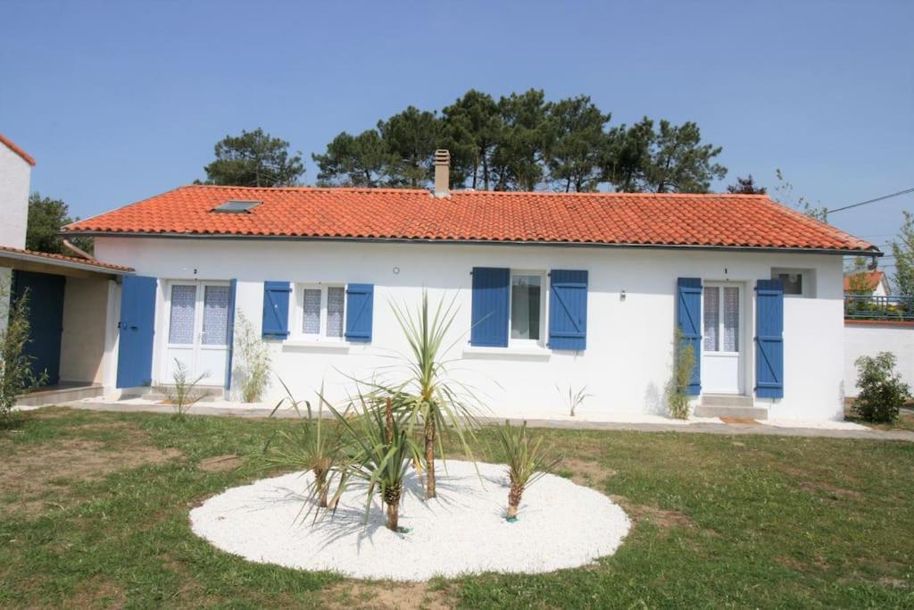 une maison blanche avec des volets bleus et des plantes dans une cour dans l'établissement Logement neuf à 750m de la plage, à La Tranche-sur-Mer