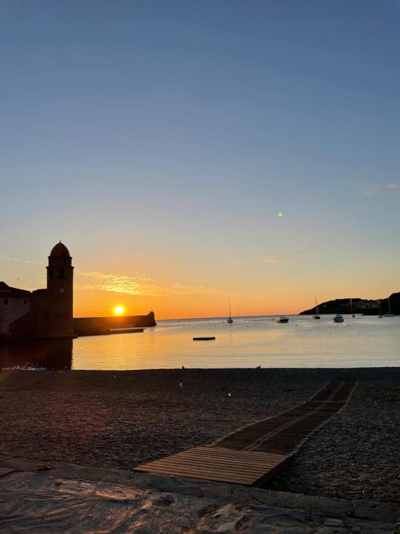 un coucher de soleil sur l'eau avec un phare sur une plage dans l'établissement Collioure Duplex, à Collioure