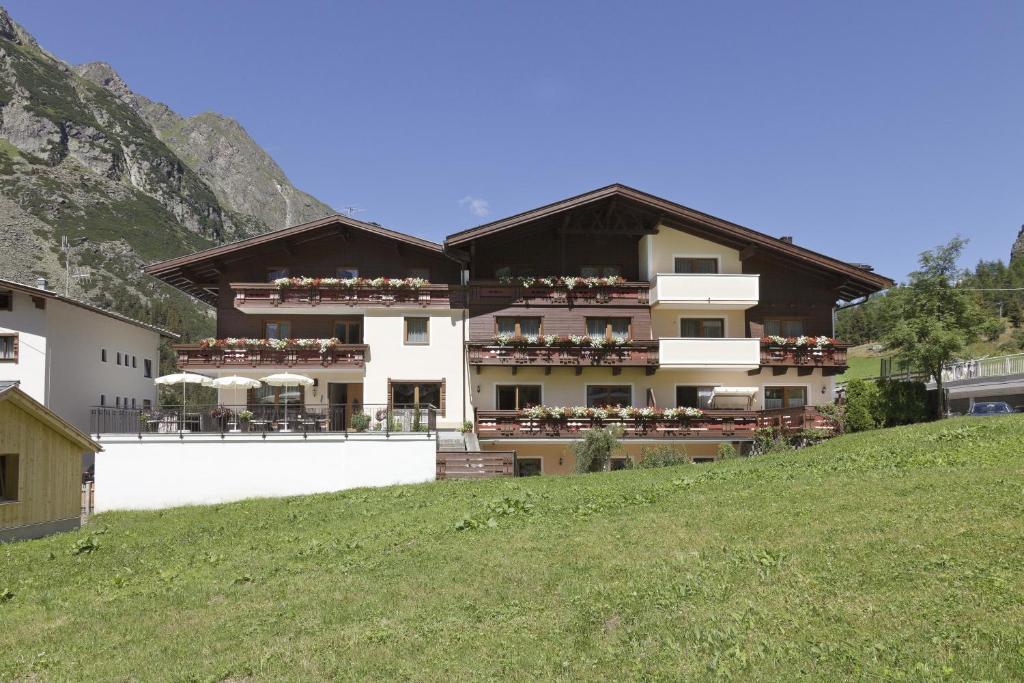 a building on a hill next to a green field at Hotel Garni Rifflsee in Sankt Leonhard im Pitztal