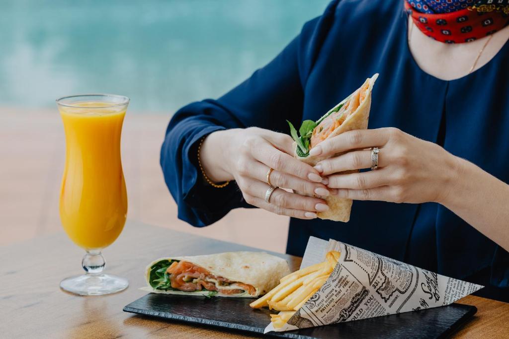 a woman holding a sandwich and a glass of orange juice at Vale d'El Rei Hotel & Villas in Carvoeiro