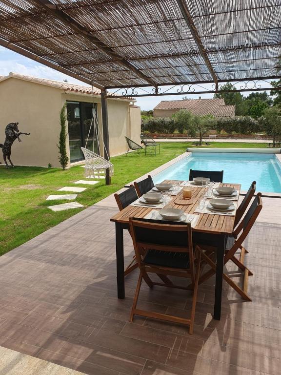 - une table en bois avec des chaises à côté de la piscine dans l'établissement La Villa Sable en Provence, à Saint-Saturnin-lès-Apt