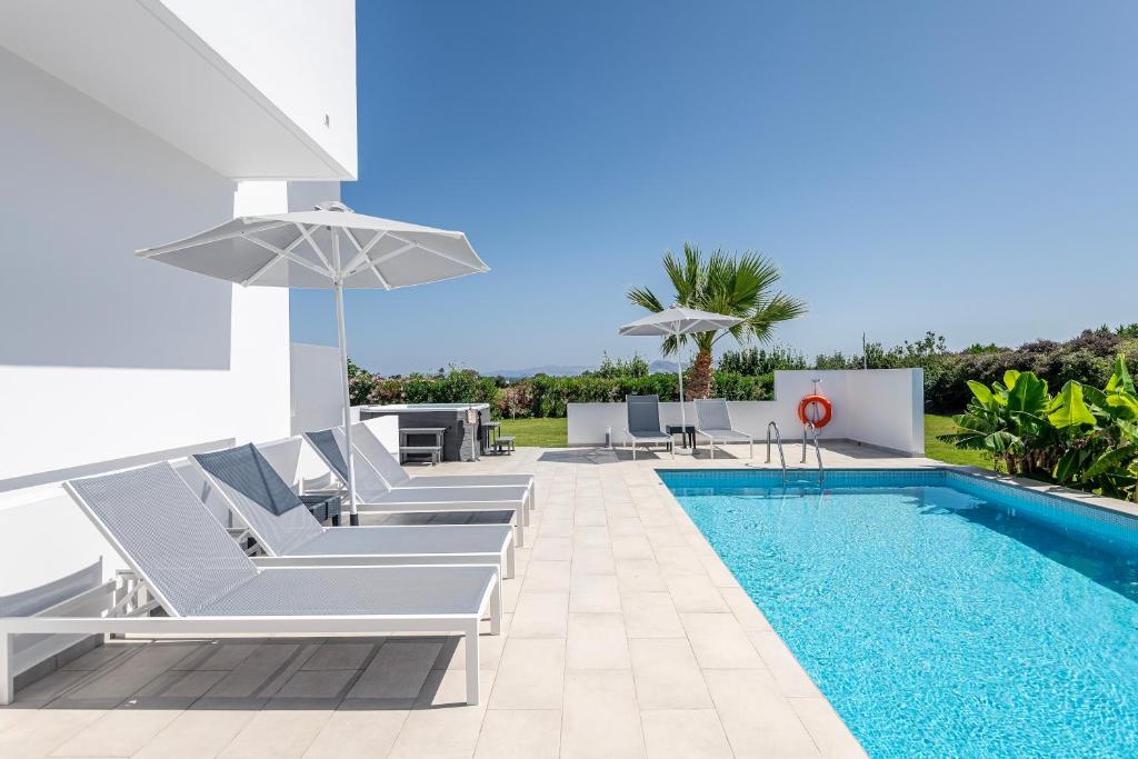 a villa with a swimming pool with chairs and an umbrella at Asteria Pearl Villa 1 with Jacuzzi in Tigaki