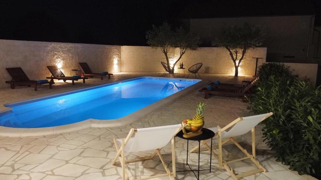 a swimming pool at night with chairs and a table at Holiday home Bevanda in Velika Čista